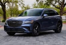Front three-quarter view of a 2027 Genesis GV70 luxury compact SUV showing its two-line headlights and long hood